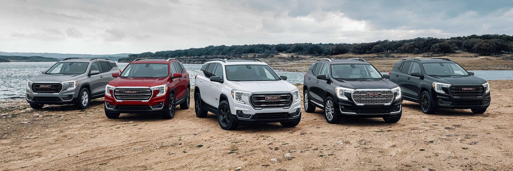 The GMC SUV models are all parked in a row on display on a dirt lakeshore 