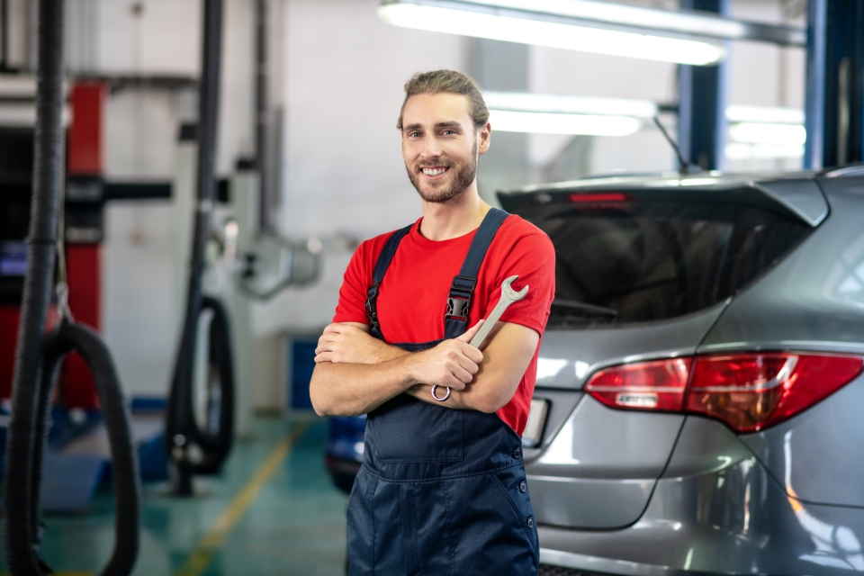 GMC Service Center certified maintenance professional wearing a red shirt and holding a wrench with crossed arms in the MADRAS, OR shop.