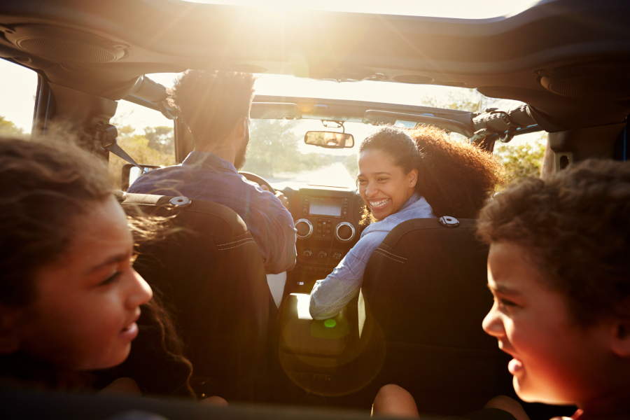 You see from behind the 2 children a laughing, care-free family with the mother looking back toward them as the father drives a GMC SUV down a beach-style road