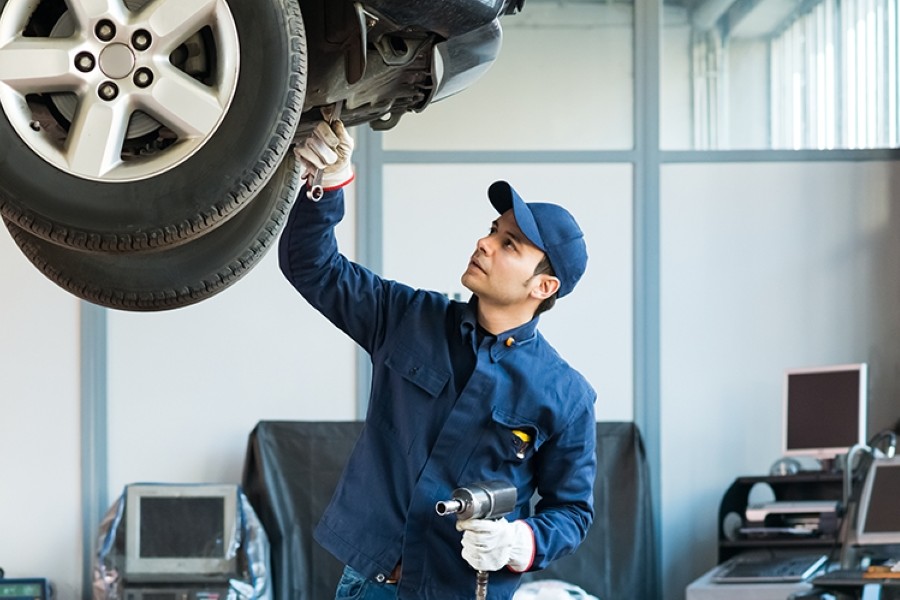 Tire inspections before summer road trip by a certified maintenance specialist with a wrench in his white gloves, blue shirt and baseball cap, adjusting the carriage above his head